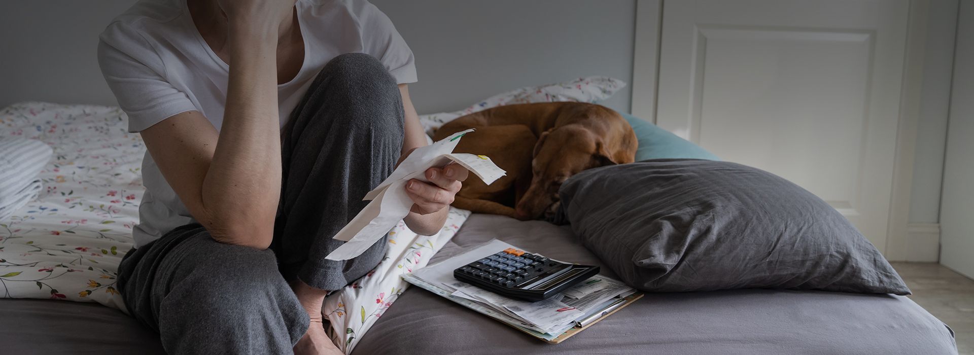 woman in pyjama sits on bed holding unpaid bills closeup